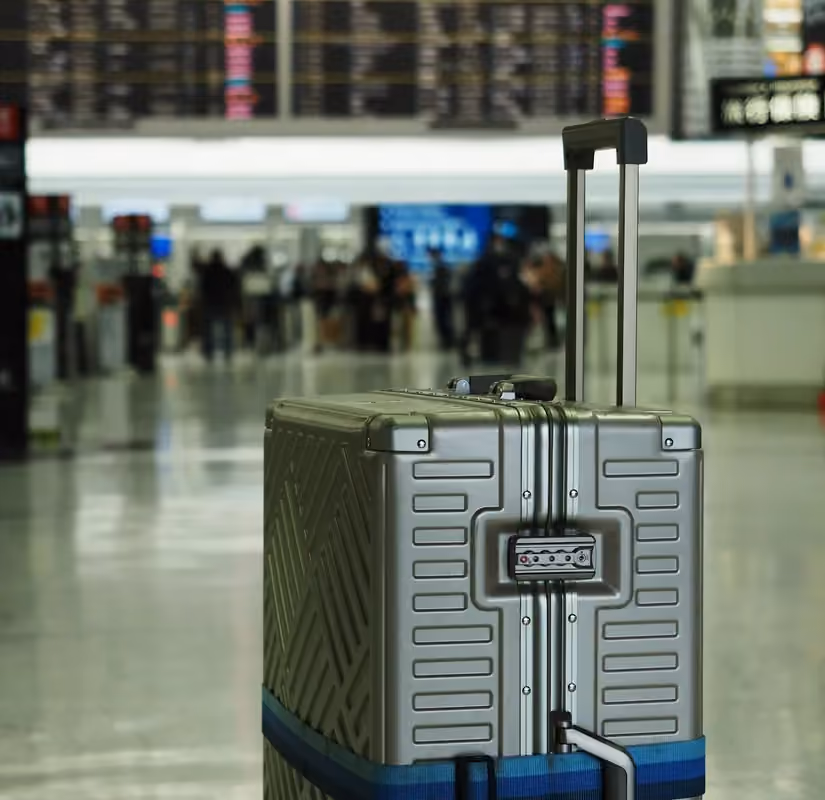 A silver suitcase with a blue strap in an airport terminal