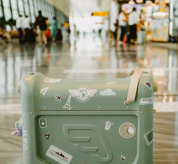A green suitcase decorated with travel stickers in a terminal